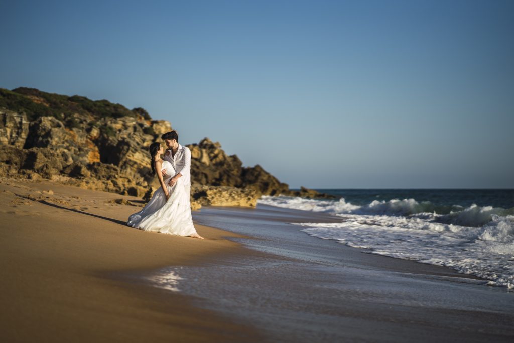 A happy caucasian loving couple wearing white hugging in the beach during a wedding photoshoot